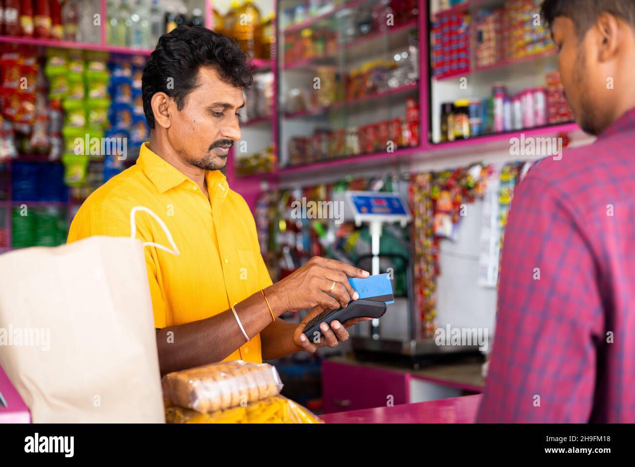 Indischer Kunde, der mit Kreditkarte im Lebensmittelgeschäft oder im Kirana-Shop bezahlt - Konzept der digitalen oder bargeldlosen Zahlung, Finanzen und Kleinunternehmen. Stockfoto