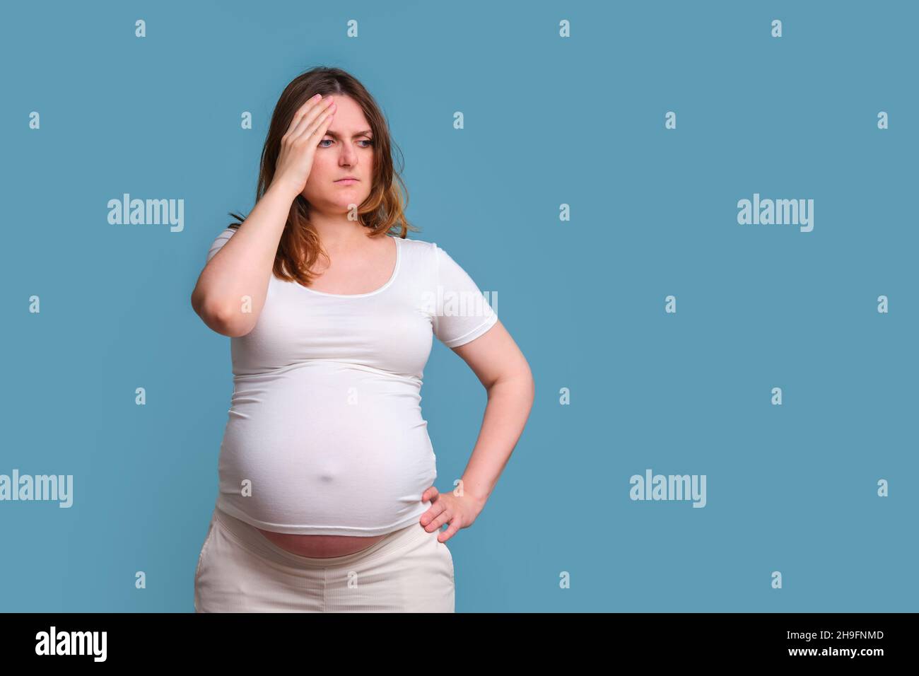 Pensivität im Gesicht einer Schwangeren, Studioaufnahme auf blauem Hintergrund Stockfoto