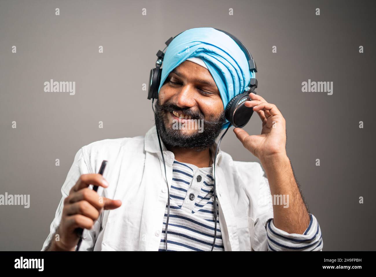 Fröhlicher junger sikh-Mann, der beim Hören von Musik auf dem Kopfhörer tanzt, indem er das Mobilephone-Konzept der freudigen Emotion und des Glücks verwendet Stockfoto