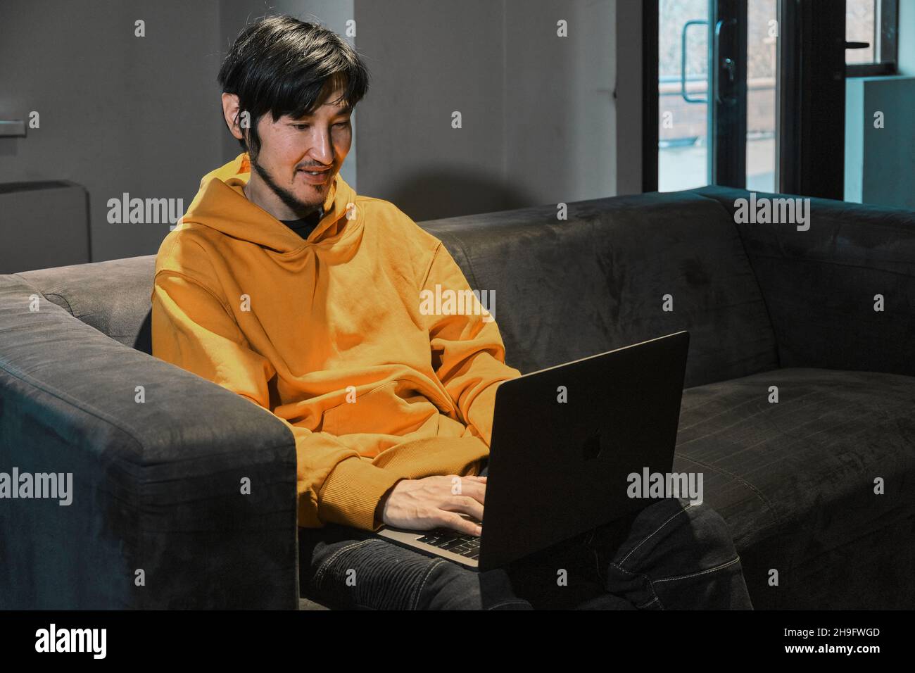 Ein Asiat sitzt in einem kleinen Büro auf dem Sofa und kommuniziert über einen Laptop über eine Videoverbindung. Das Konzept von Kleinunternehmen und Online-Kommunikation. Stockfoto