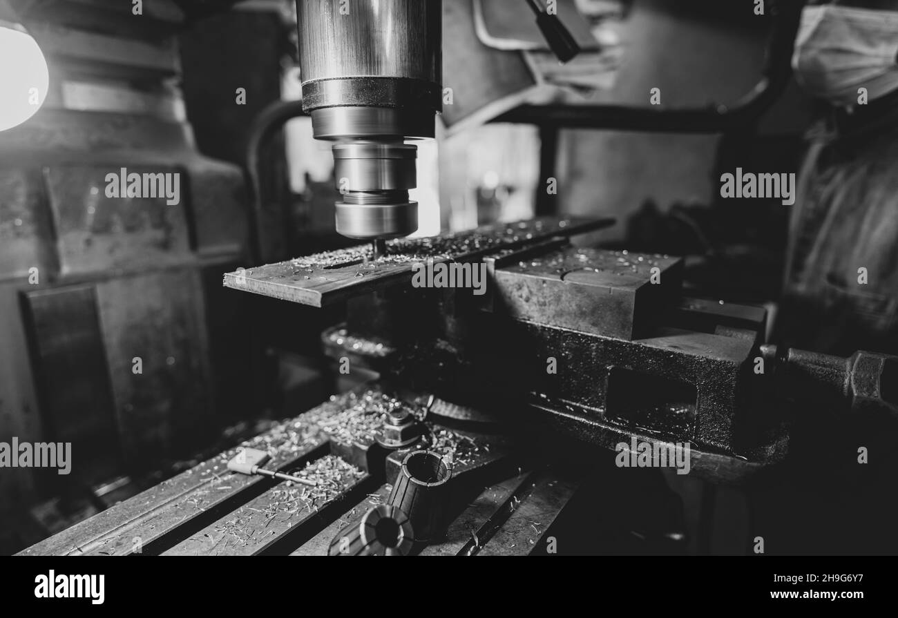 Fräsmaschine, die in der Nähe des Arbeiters mit einer Schutzmaske arbeitet. Werkzeug zum Schneiden von Metallwerkstücken. Vertikale Fräsmaschine mit Wolfram Hartmetall Fräsen Stockfoto