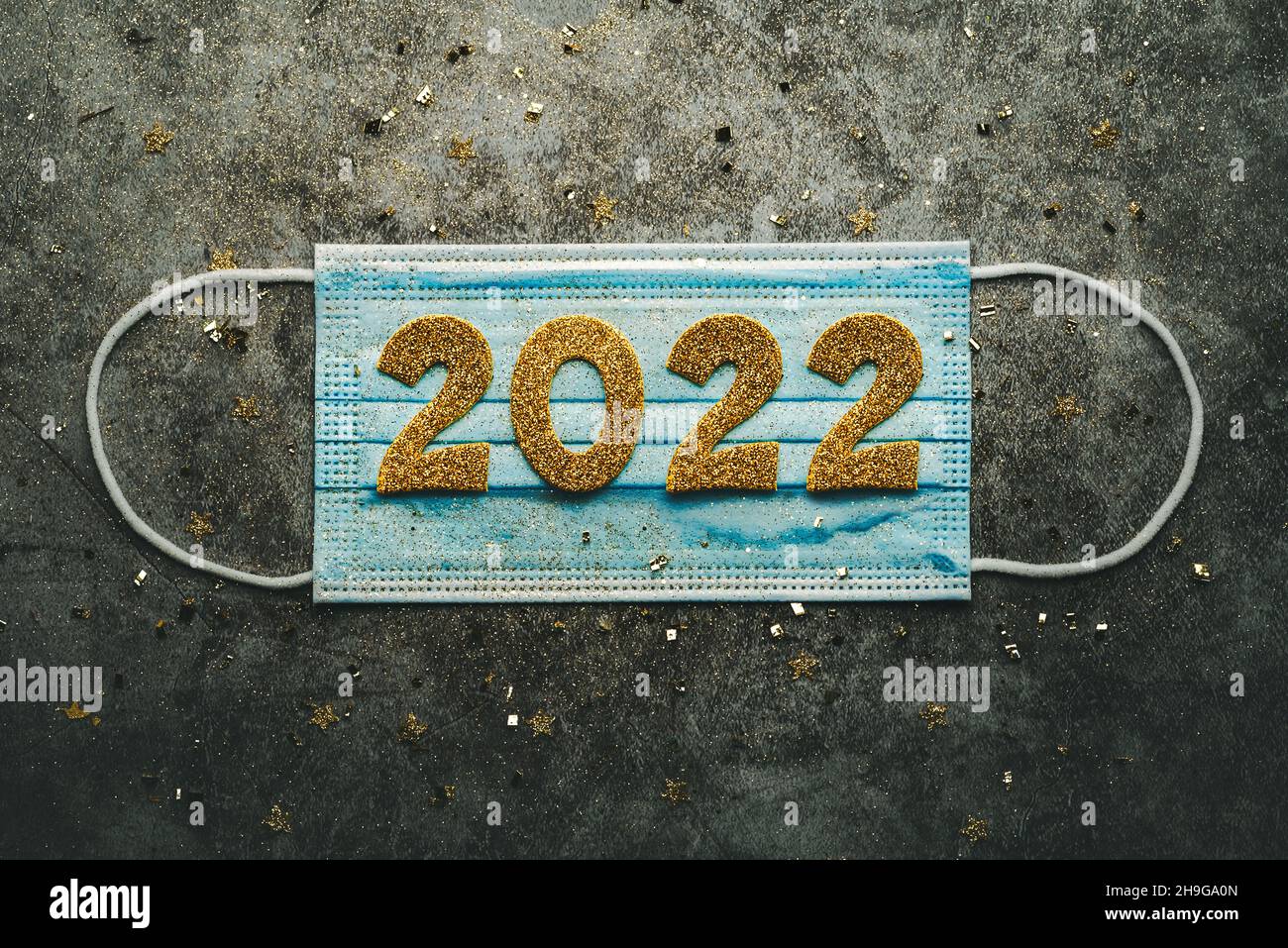 Silvester Feier Konzept Hintergrund.Medizinische Maske mit den Zahlen 2022 auf grauem Hintergrund. Covid-19 Neujahrskonzept Stockfoto