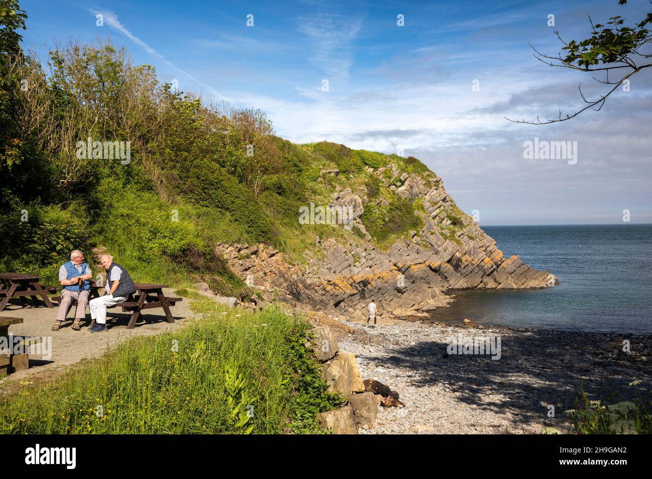 Großbritannien, Wales, Pembrokeshire, Stackpole Quay, Männer, die sich bei Sonnenschein auf dem Picknicktisch an der Küste entspannen Stockfoto