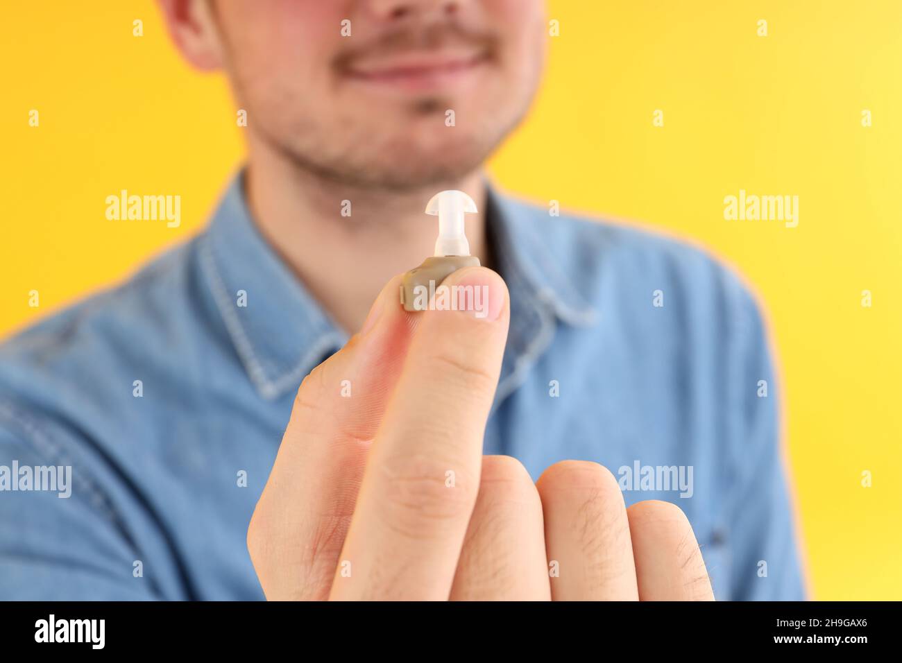 Junger Mann hält Hörgeräte auf gelbem Hintergrund Stockfoto