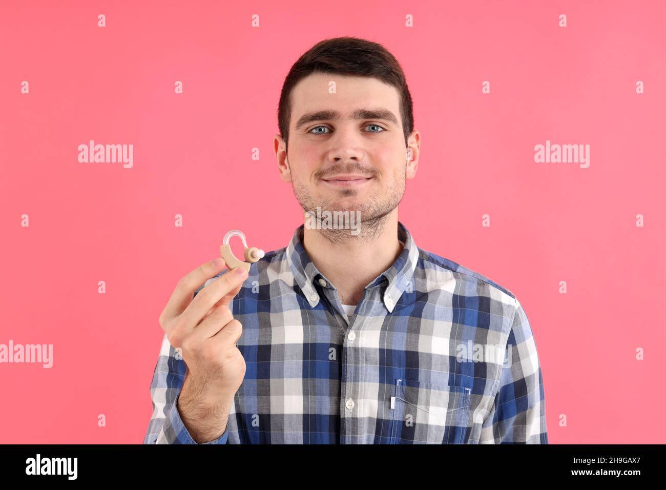 Junger Mann hält Hörgeräte auf rosa Hintergrund Stockfoto