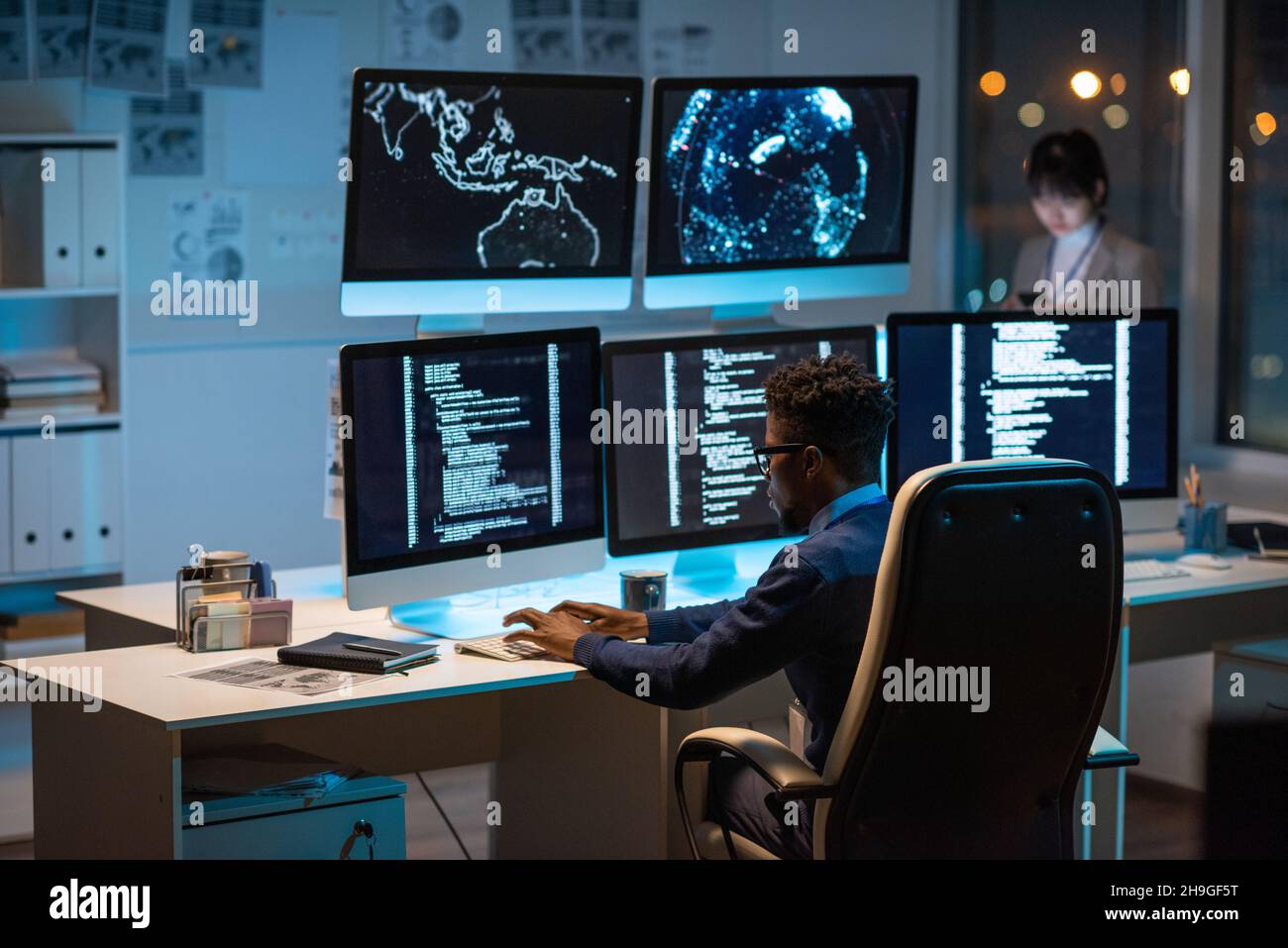 Der junge, moderne Cyber-Sicherheitsmanager tippt am Schreibtisch vor Computermonitoren Stockfoto