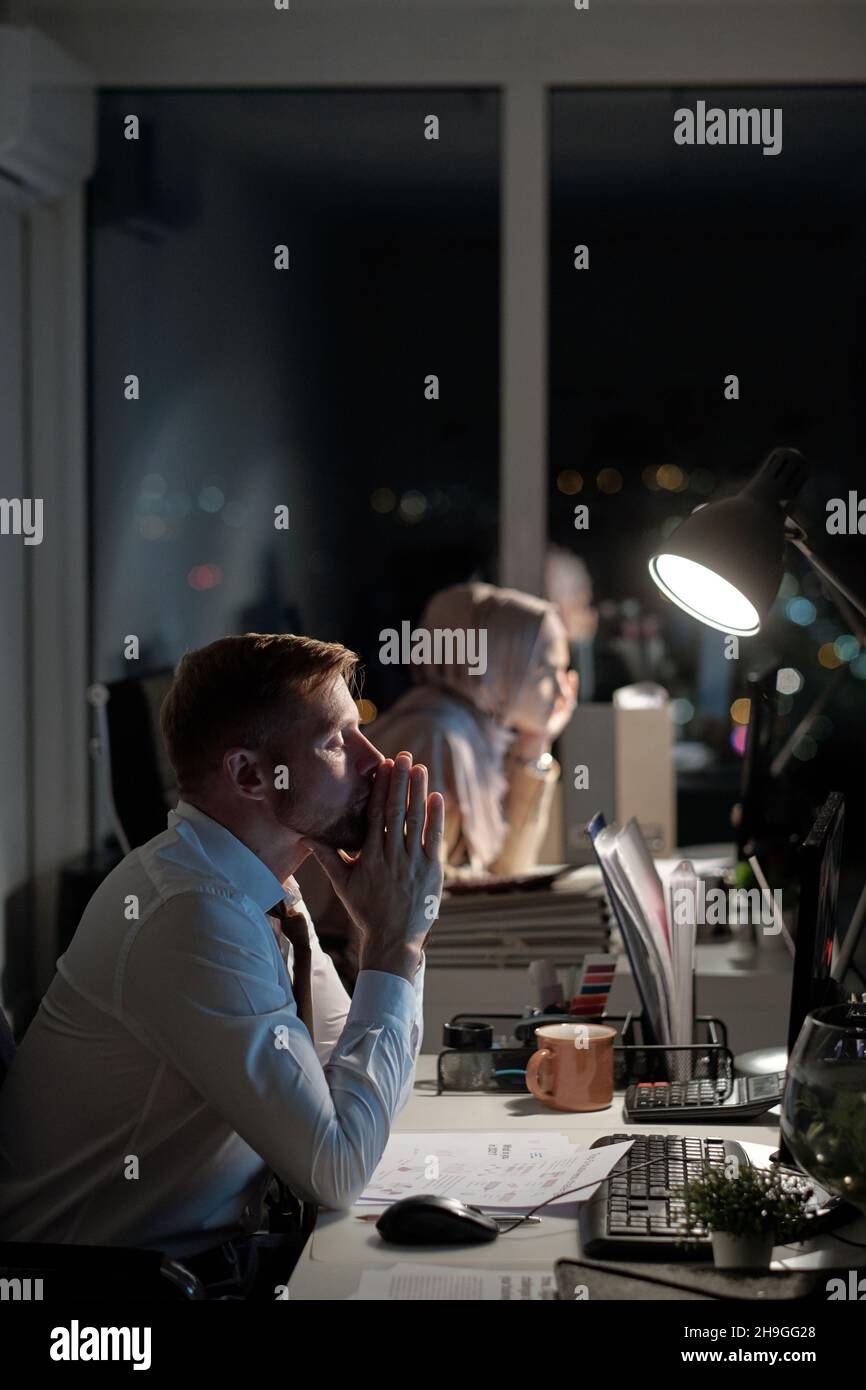 Müder Geschäftsmann, der seine Hände im Gesicht zusammengelegt vor dem Computermonitor gegen eine Kollegin sitzt Stockfoto