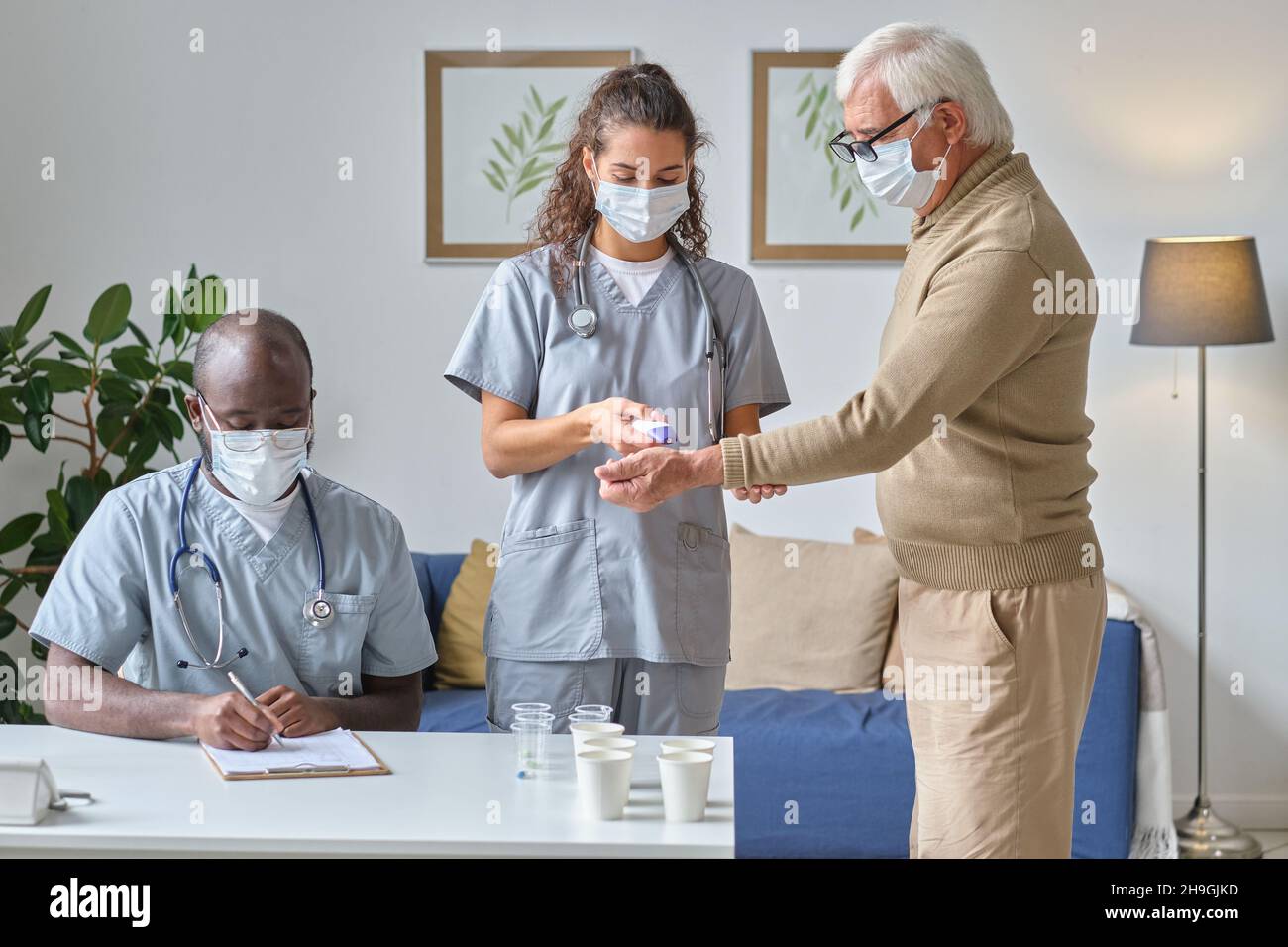 Krankenschwester, die den Patienten mit speziellen medizinischen Geräten untersucht, wobei der Arzt am Tisch sitzt und sich während der medizinischen Untersuchung Notizen macht Stockfoto