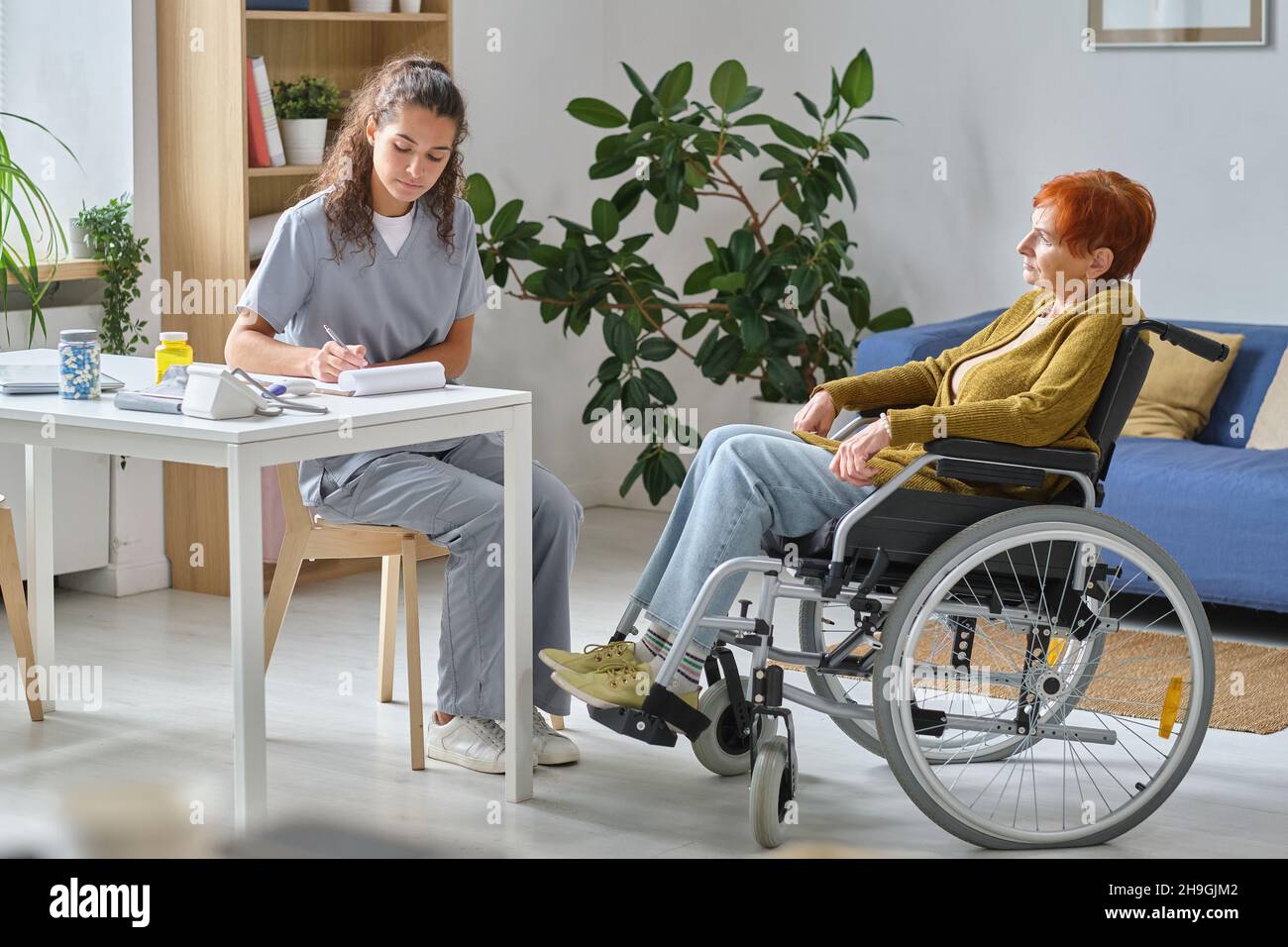 Ärztin, die die Behandlung für ältere Frauen verschreibt, die im Rollstuhl sitzen und einen Arzt im Krankenhaus besuchen Stockfoto