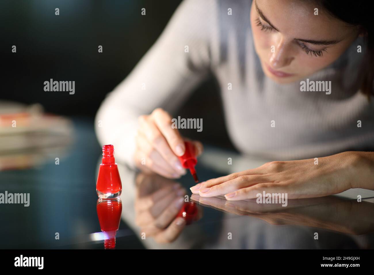 Konzentrierte Frau malen Nägel in rot zu Hause in der Nacht Stockfoto