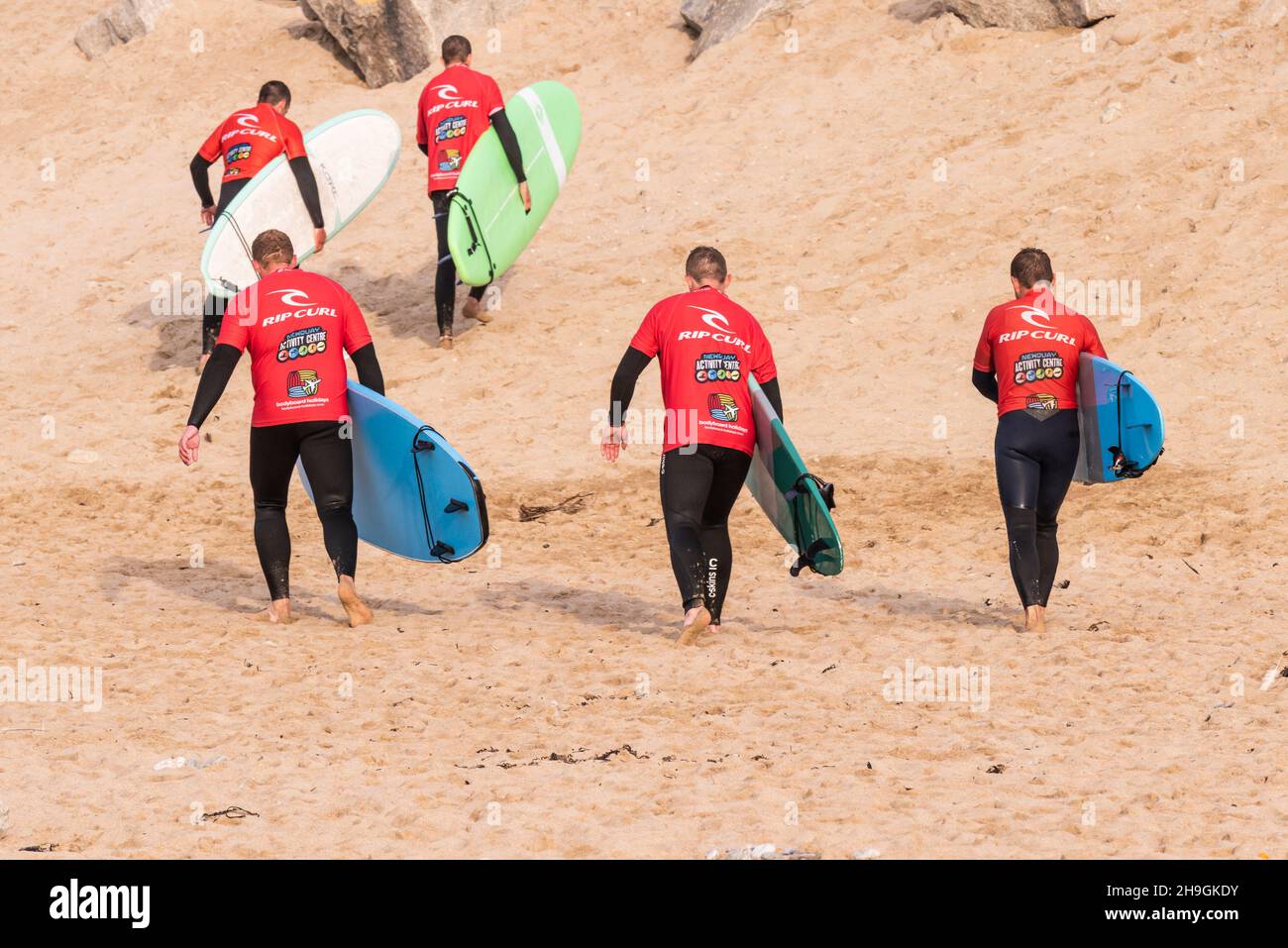 Eine Gruppe männlicher Surfer, die ihre gemieteten Surfbretter zum Surf-Verleih in Fistral in Newquay in Cornwall zurückbringen. Stockfoto