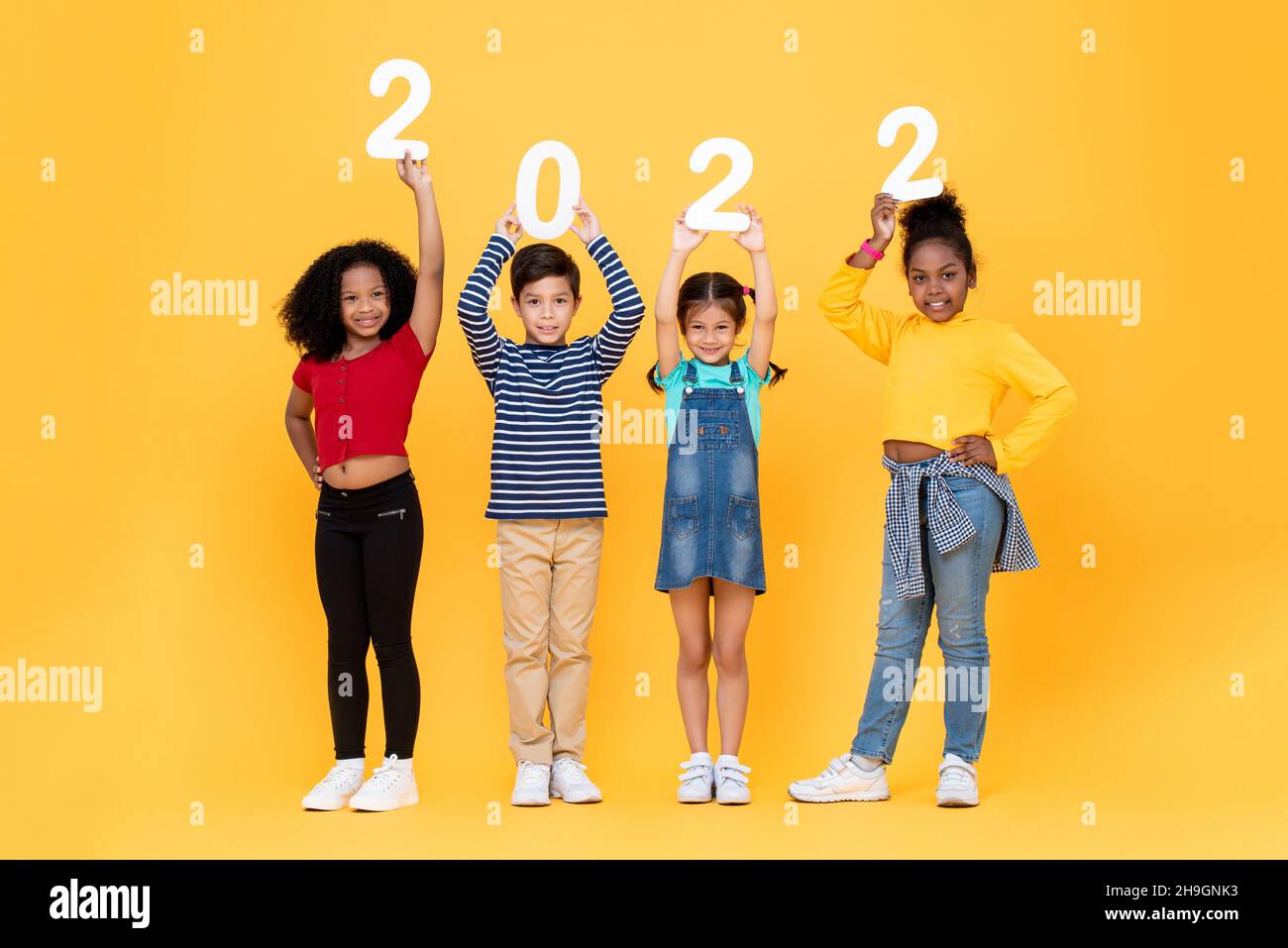 Glückliche nette kleine Kinder lächeln und halten 2022 Zahlen isoliert auf gelben Studio-Hintergrund für Neujahr Konzepte Stockfoto