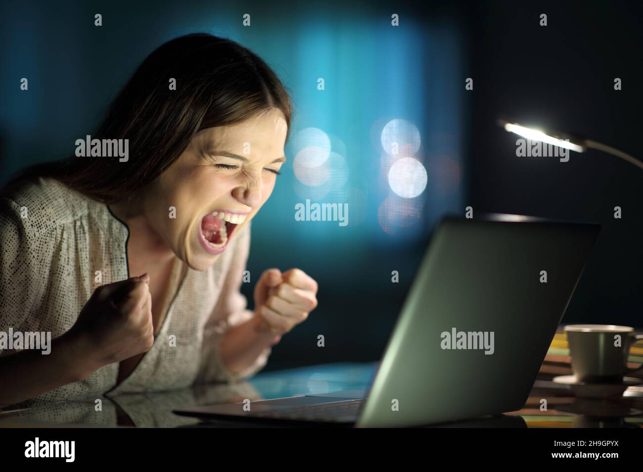 Aufgeregte Frau, die nachts zu Hause auf dem Laptop nachcheckt Stockfoto