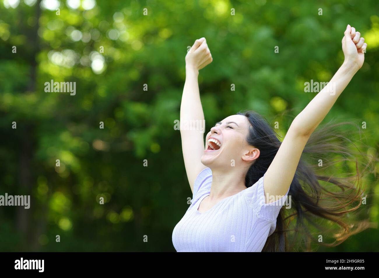 Aufgeregt asiatische Frau, die die Arme hebt und den Erfolg in einem Park feiert Stockfoto