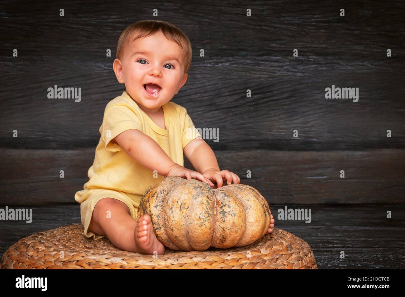 Niedliches Baby mit dem Kürbis lächelnd auf dem Strohtisch auf dem Holzhintergrund Stockfoto