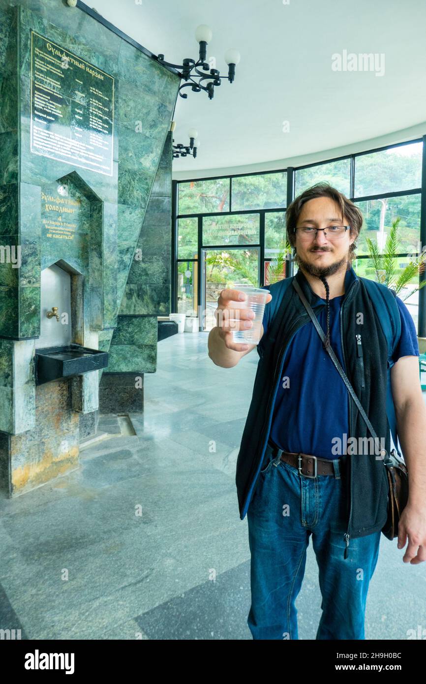 Ein Mann gibt Mineralthermalwasser in den Einweg-Becher im Pumpenraum, Nahaufnahme. Narzan-Quelle in Kislowodsk, Russland. Hochwertige Fotos Stockfoto