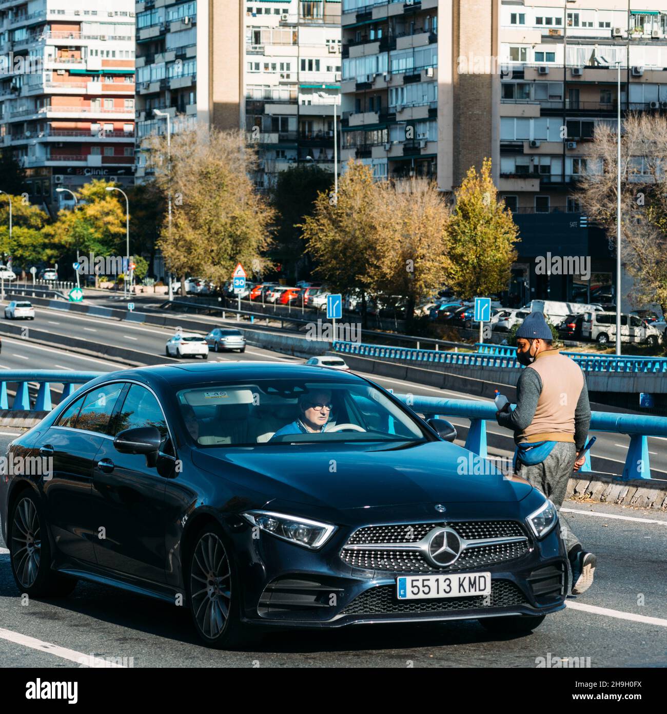 Mann mittleren Alters mit südasiatischem Aussehen, der in Madrid, Spanien, Autoscheiben mit einem Scheibenwischer (Abstreifer) waschte. Autobahn M30 Stockfoto