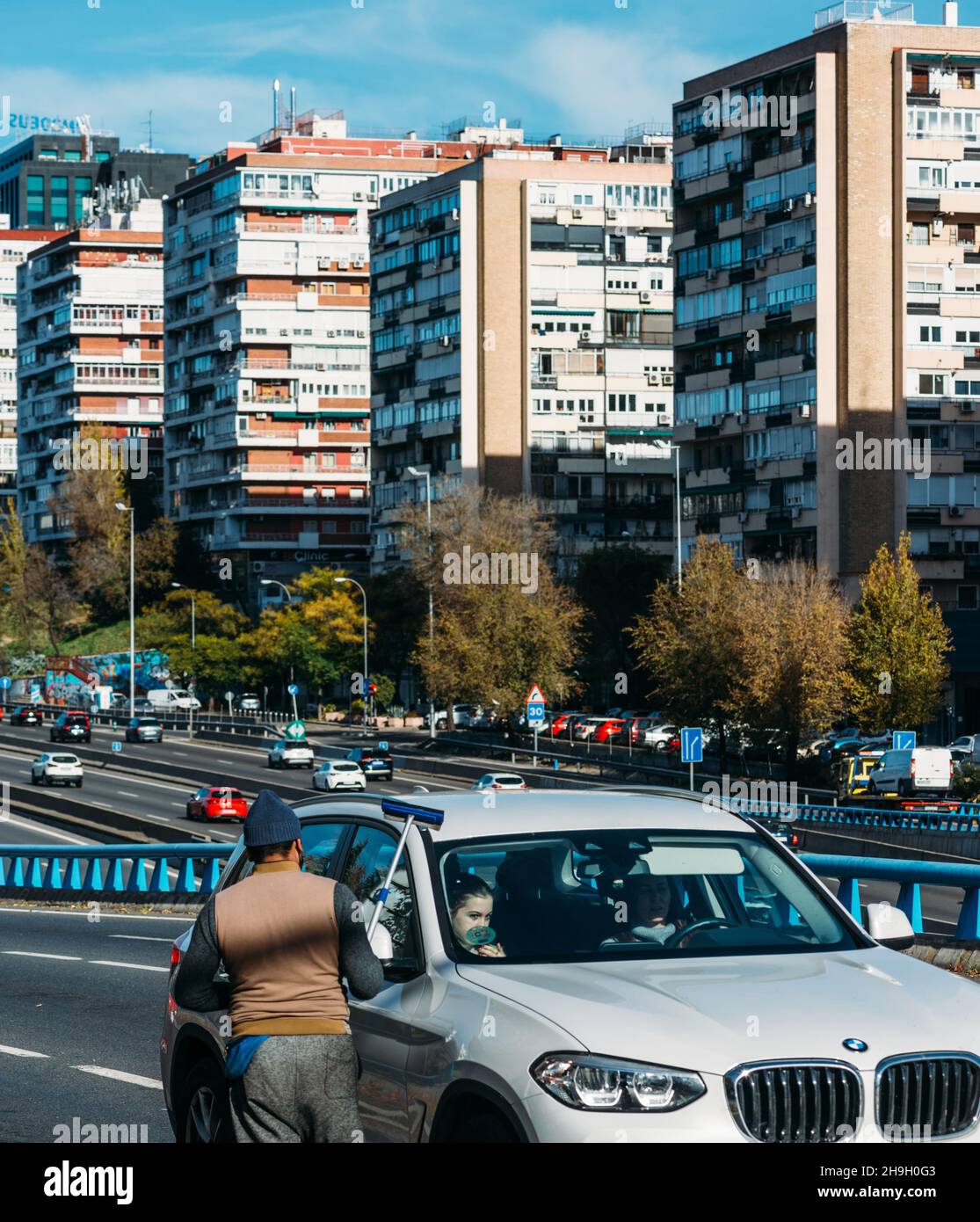 Mann mittleren Alters mit südasiatischem Aussehen, der in Madrid, Spanien, Autoscheiben mit einem Scheibenwischer (Abstreifer) waschte. Autobahn M30 Stockfoto