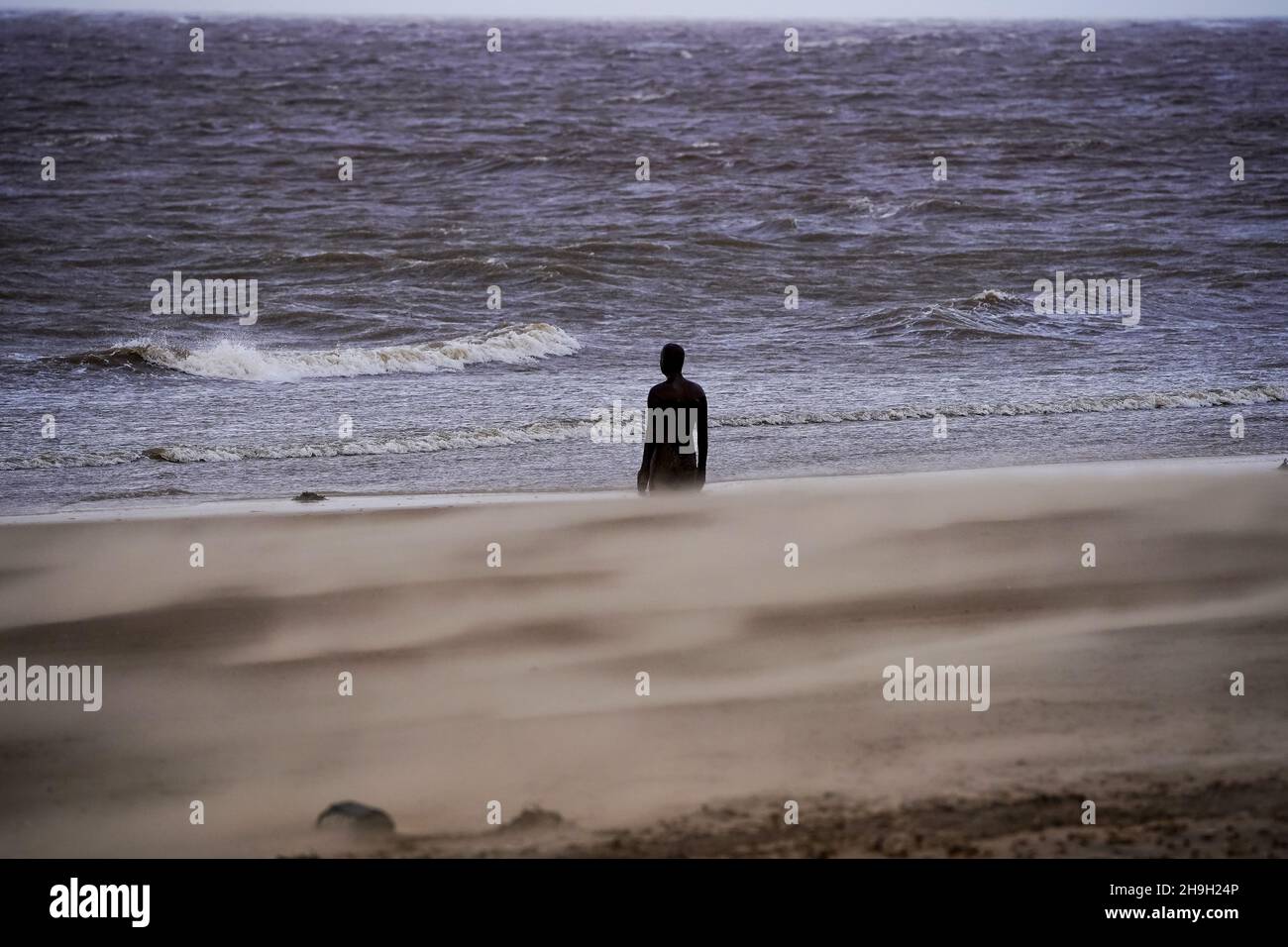 Sand weht an einer der Anthony Gormley-Statuen vorbei, die „Another Place“ am Crosby Beach Merseyside genannt wird, als der Sturm Barra am Dienstag Großbritannien und Irland mit störenden Winden, starkem Regen und Schnee traf. Bilddatum: Dienstag, 7. Dezember 2021. Stockfoto