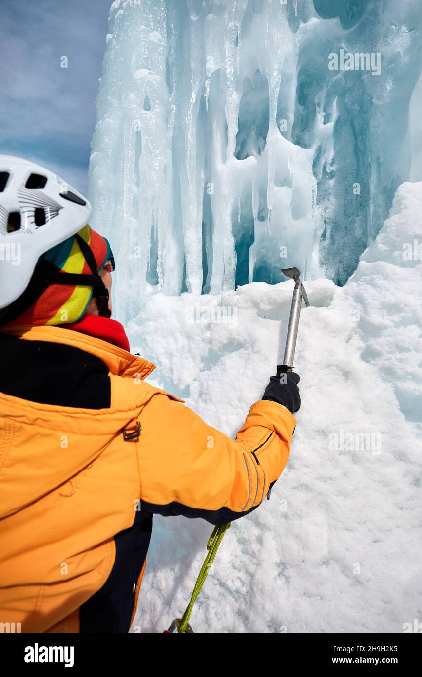 Frau Kletterin mit Eispickel in oranger Jacke in der Nähe von gefrorenen Wasserfall in den Bergen in Almaty, Kasachstan Stockfoto
