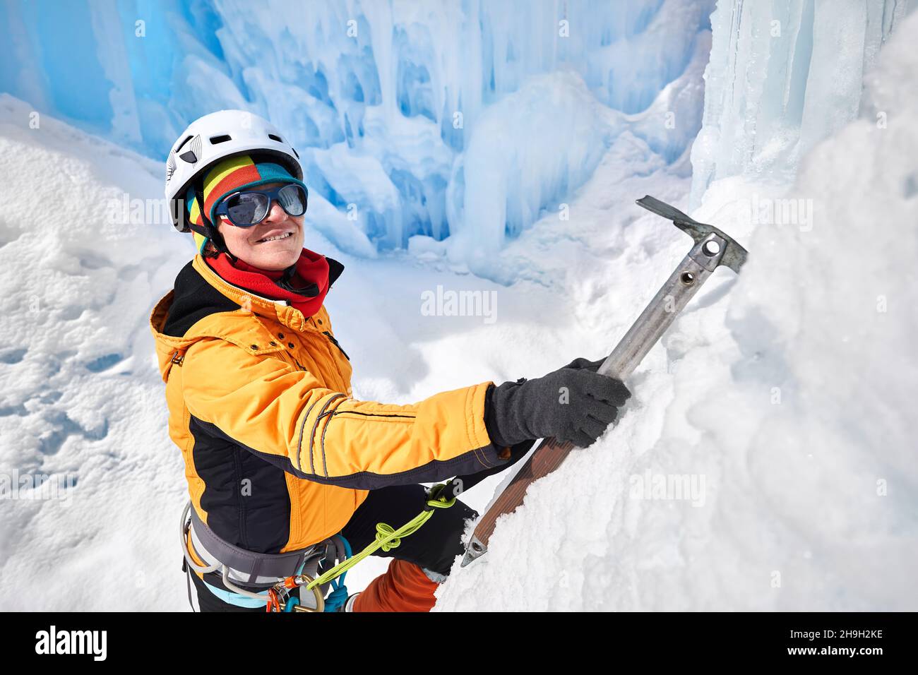Frau Kletterin in oranger Jacke mit Eispickel in der Nähe von gefrorenen Wasserfall in den Bergen in Almaty, Kasachstan Stockfoto
