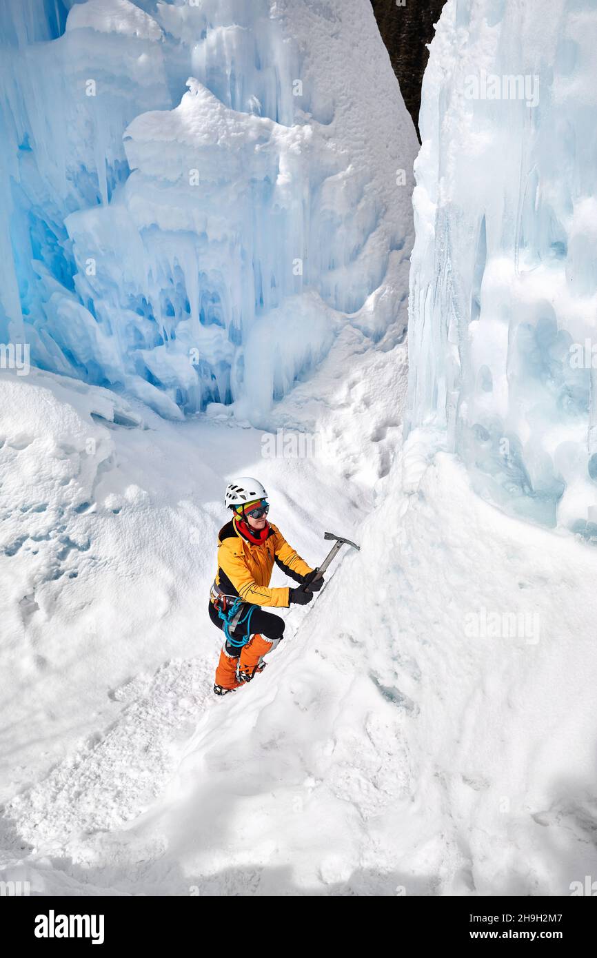Frau Kletterin in oranger Jacke mit Eispickel in der Nähe von gefrorenen Wasserfall in den Bergen in Almaty, Kasachstan Stockfoto