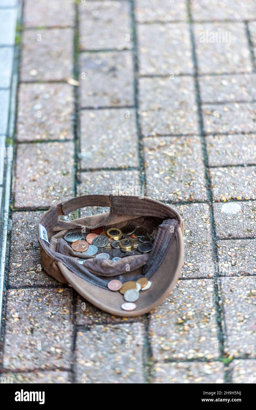 Eine flache Mütze wurde auf dem Bürgersteig von einem Mann hinterlassen, der bettelte, Obdachlosigkeit hatte und auf der Straße um Geld bettelte, schlafender, rauer Bettler, der mit Mütze um Geld bat. Stockfoto