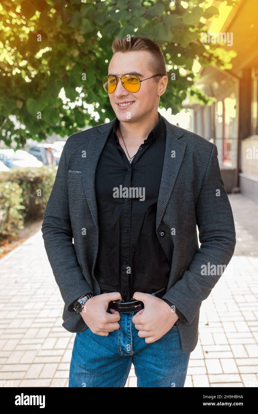 Stylish positiv lächelnd jung attraktiv Kerl des europäischen Auftritts Geschäftsmann Porträt in Jacke, Hemd und Jeans, in Sonnenbrille auf der Straße outd Stockfoto