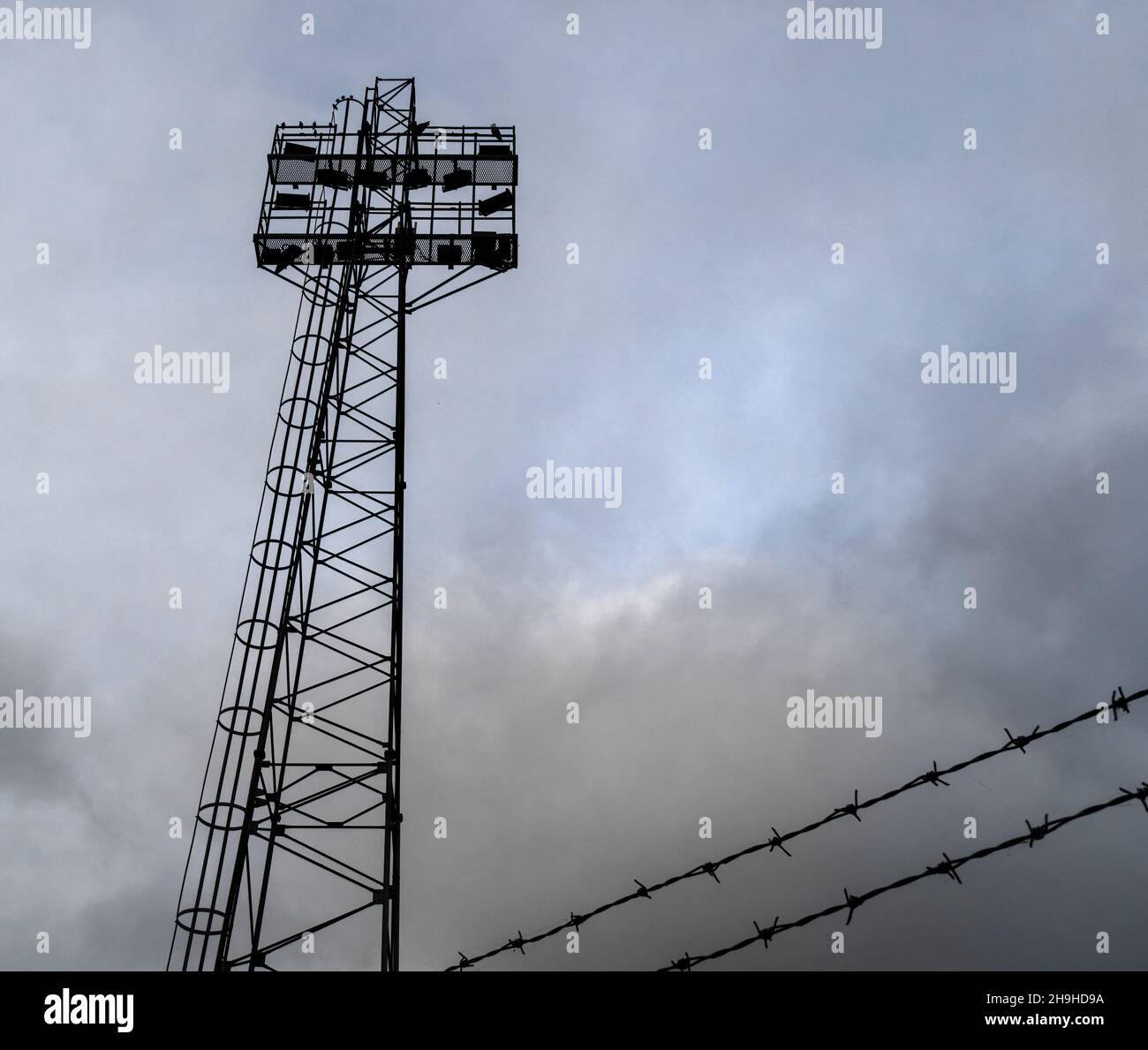 Flutlichter im Sportstadion und Stacheldraht vor stürmischem Himmel. Stockfoto