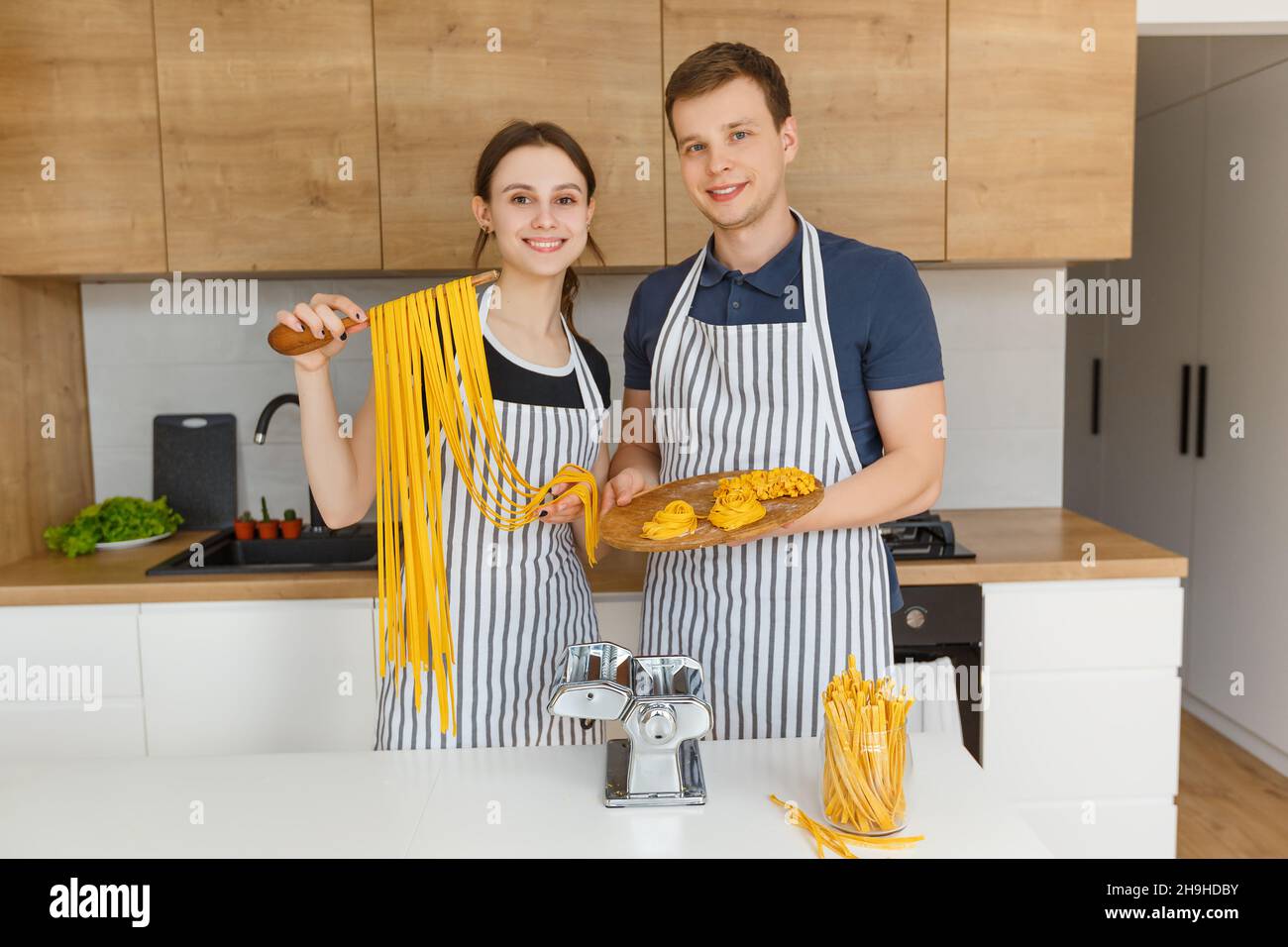 Porträt eines jungen Paares in Schürzen, das rohe Nudelnudeln hält. Familienküche italienische vegane Küche zu Hause. Konzept der häuslichen Lebensweise, gesunde Ernährung Stockfoto