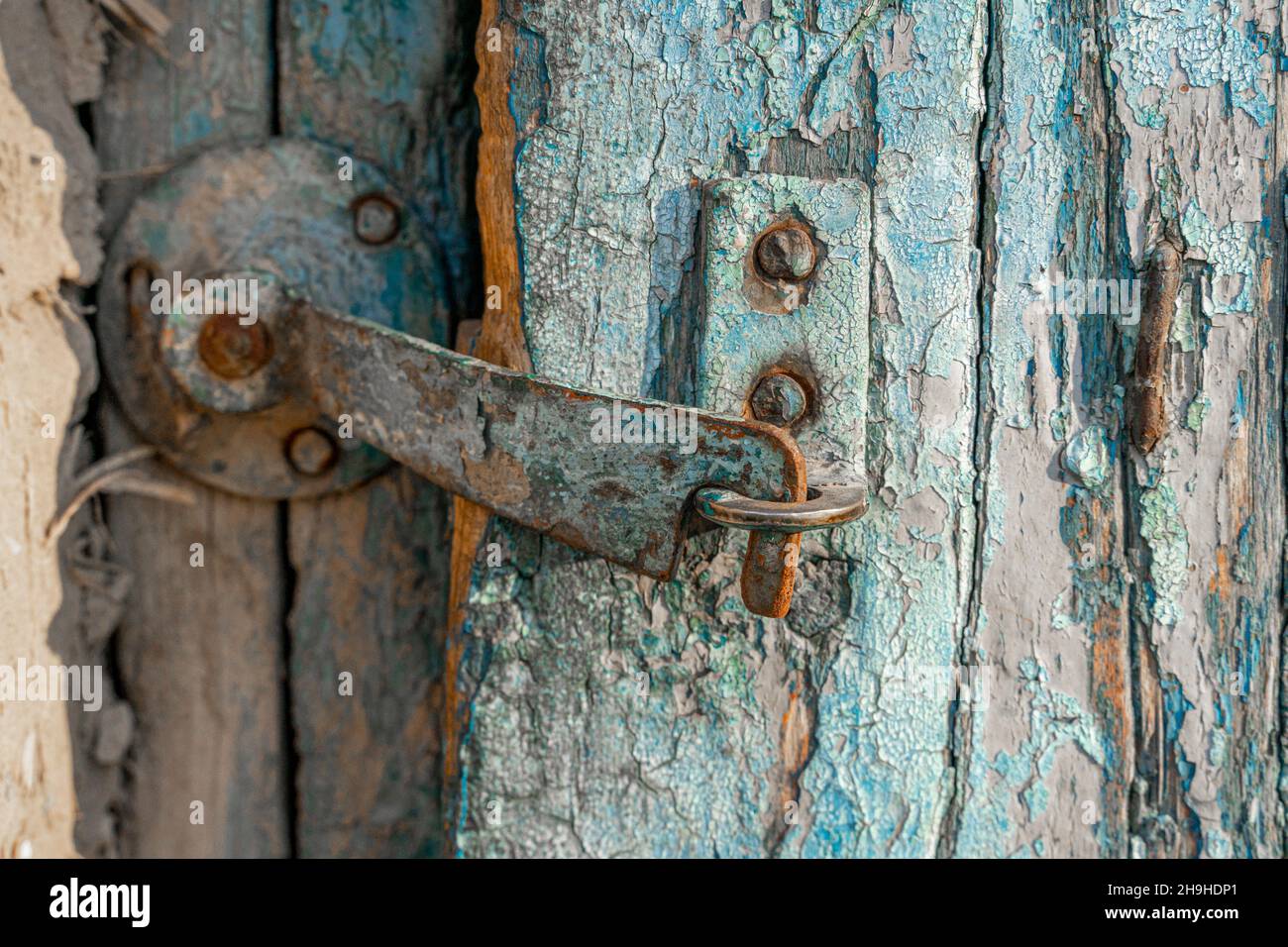 Ein rostiger Metallriegel, mit Farbe geschält, schnappte sich an einer alten Holztür mit verwitterter Farbe Stockfoto