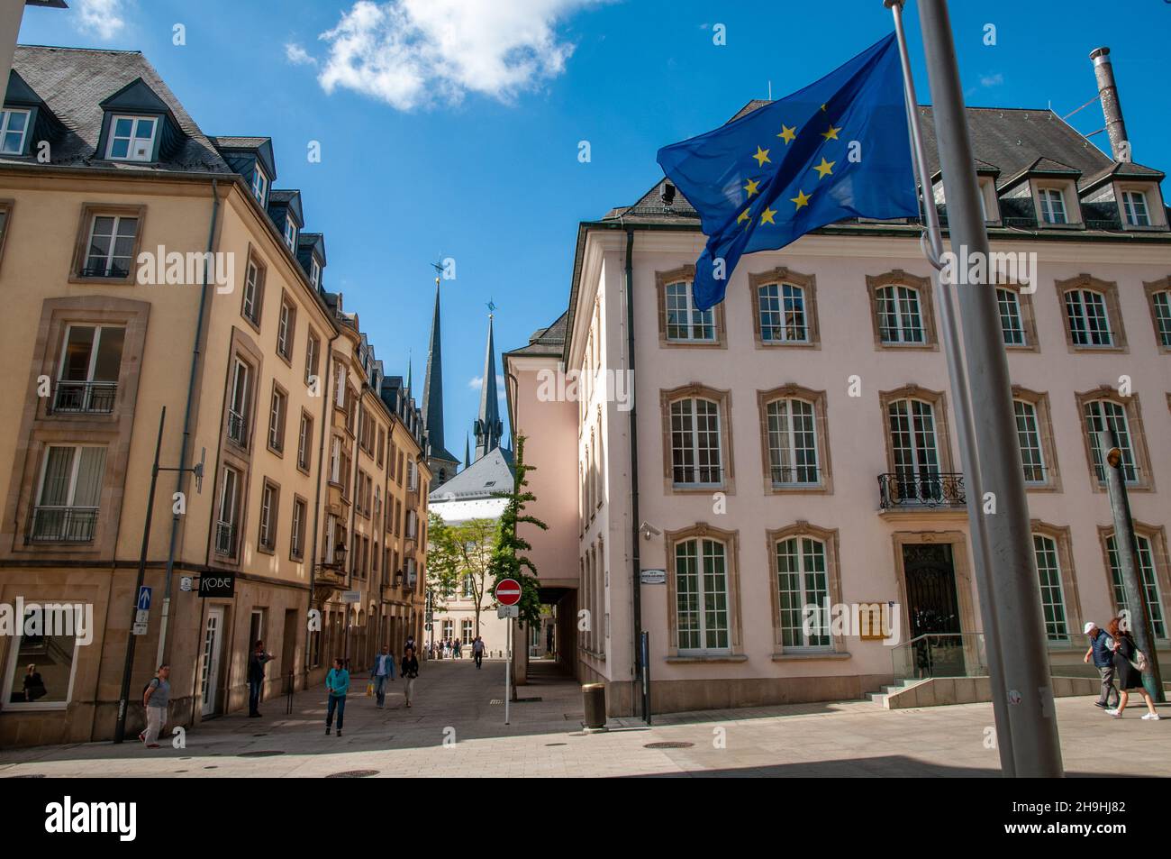 Die EU-Flagge der Abgeordnetenkammer in der Rue du Marché-aux-Herbes in Luxemburg-Stadt mit den Türmen der Kathedrale Notre-Dame in der Ferne. Stockfoto