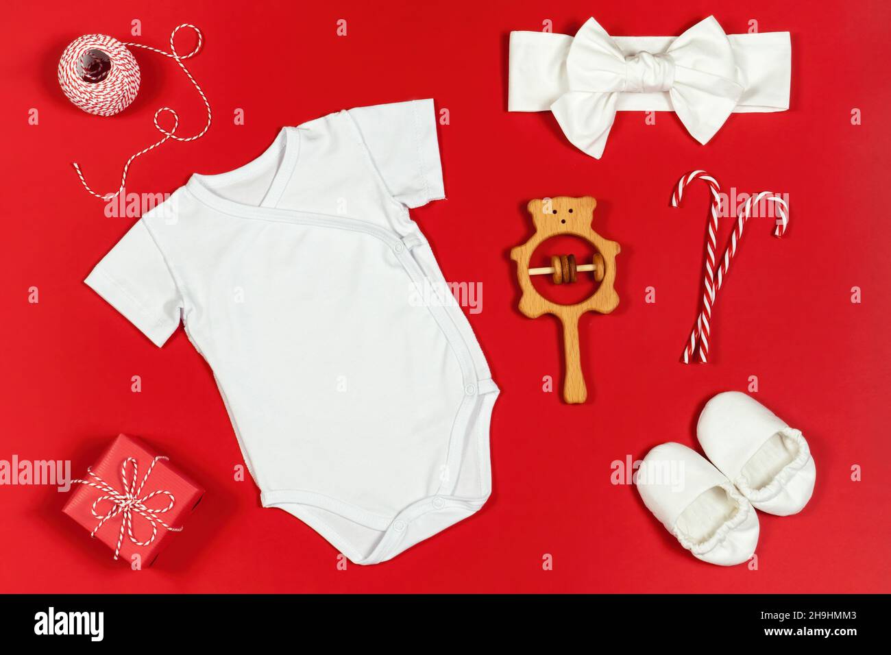 Neugeborenes Baby Kleidung Mockup auf weihnachten Hintergrund. Baby Bodysuite Mockup mit Booties, Stirnband und weihnachtsschmuck auf rotem Hintergrund. Stockfoto