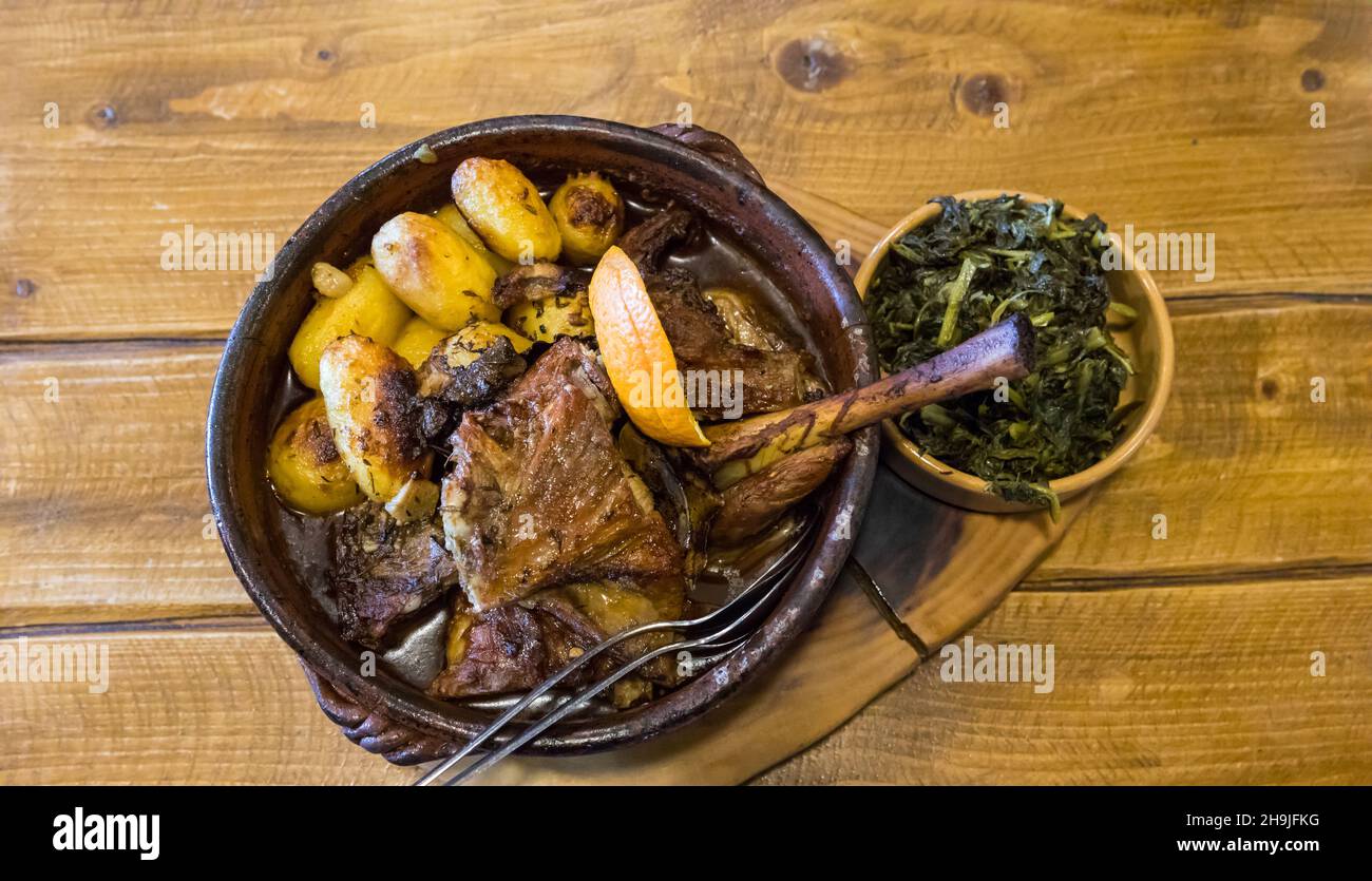 Gebratener Ziegenbock oder geröstetes Kind „cabrito assado“, bereit zum Essen auf einem Holztisch. Serviert mit gerösteten Kartoffeln und Sprossen. Typisch portugiesisches Gericht Stockfoto