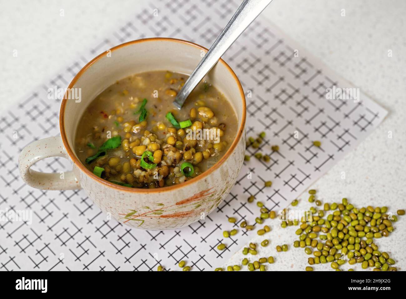 Mungo-Bohnen-Suppe in Schüssel mit Löffel, trockener mungo-Samen (vigna radiata) auf Tisch. Stockfoto