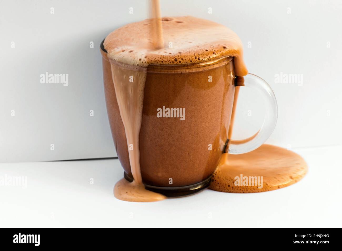 Überfließendes und schaumig schaumendes Schokoladengetränk im Glas auf weißem Hintergrund. Ausgezeichnetes Getränk, das sich im Winter erwärmt. Stockfoto