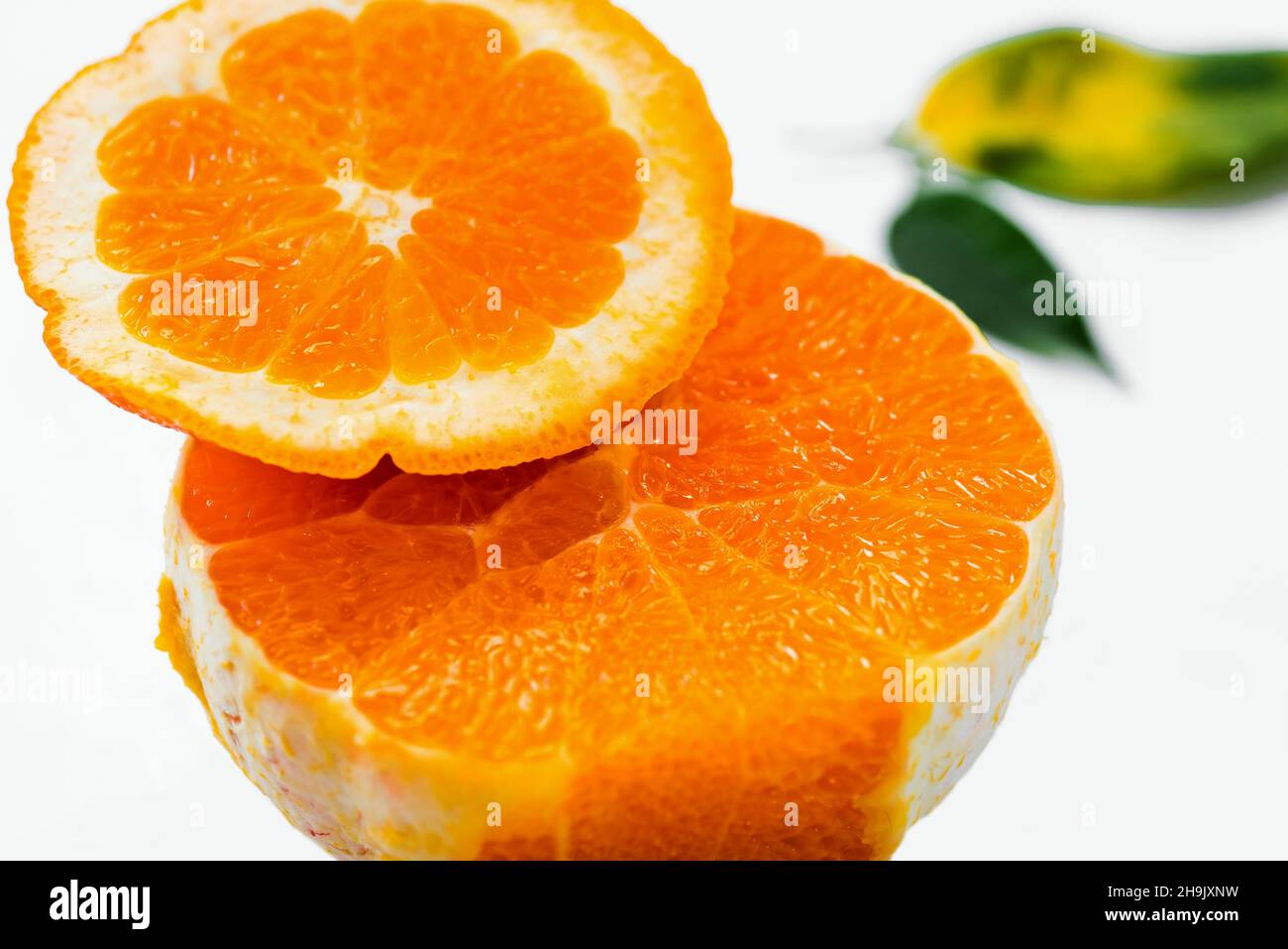 Halbiert geschälte frische Orange (schöne Struktur aus orangefarbenem Fleisch) mit verschwommenem Blatt auf weißem Hintergrund, Nahaufnahme. Stockfoto