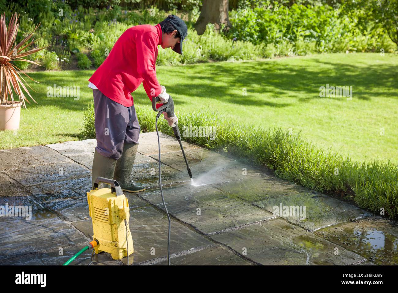 Jet-Washing auf der Terrasse. Frau Hochdruckwäsche, Powerwäsche oder Reinigung einer Gartenterrasse, Großbritannien Stockfoto