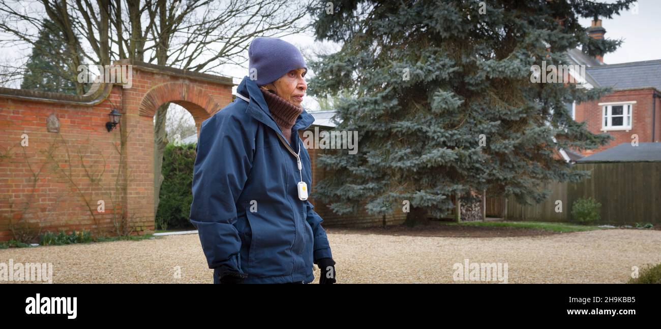 Alte indische Frau in Winterkleidung und persönlichem Sicherheitsalarm-Anhänger, zu Fuß außerhalb, Großbritannien Stockfoto