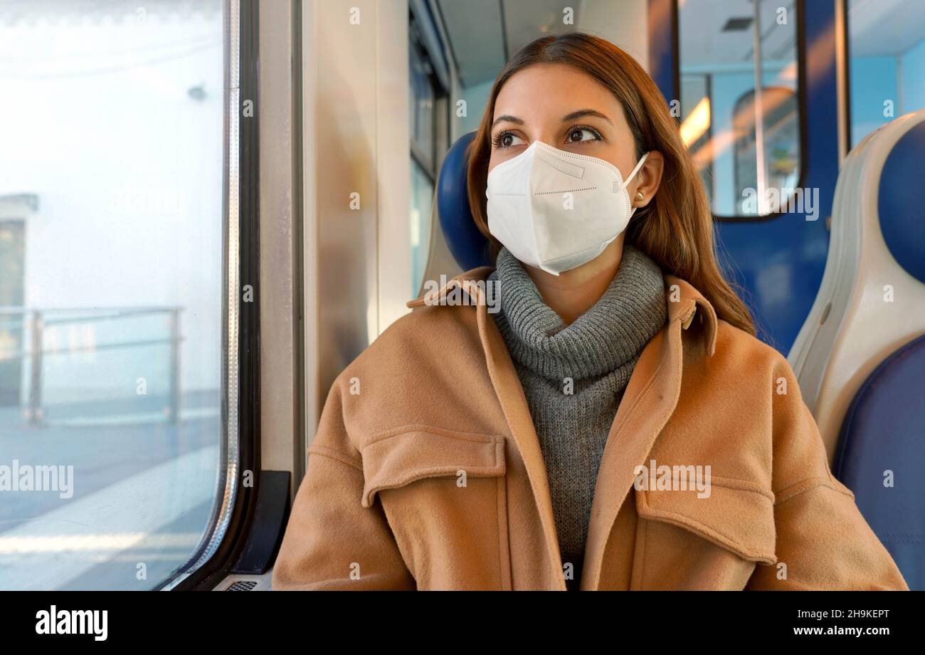 Fahren Sie sicher mit öffentlichen Verkehrsmitteln. Junge Frau mit KN95 FFP2 Gesichtsmaske, die durch das Zugfenster schaut. Pendler-Passagier mit Schutzmaske reist Stockfoto