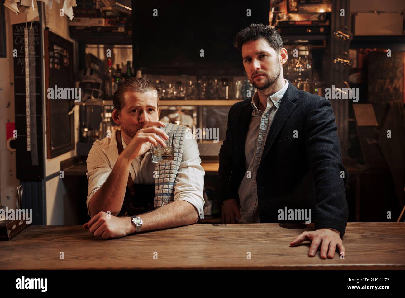 Kaukasischer Barkeeper und männlicher Gast, der an der Bar steht und aus Whiskey-Glas trinkt Stockfoto