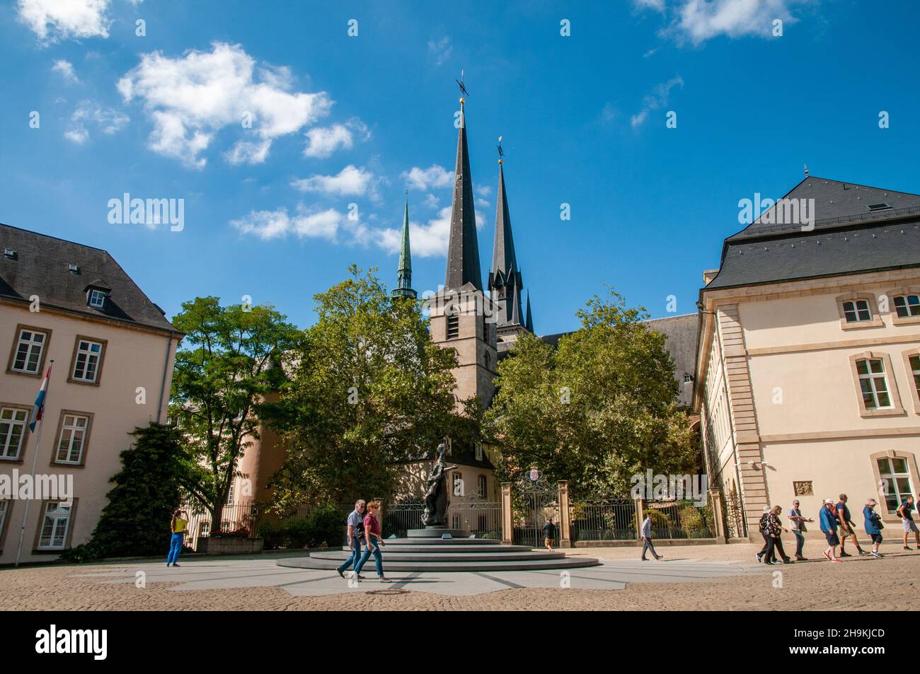 Menschen, die im Sonnenschein auf dem Clairefontaine-Platz mit der Kathedrale Notre-Dame und ihren drei Türmen im historischen Zentrum von Luxemburg-Stadt spazieren. Stockfoto