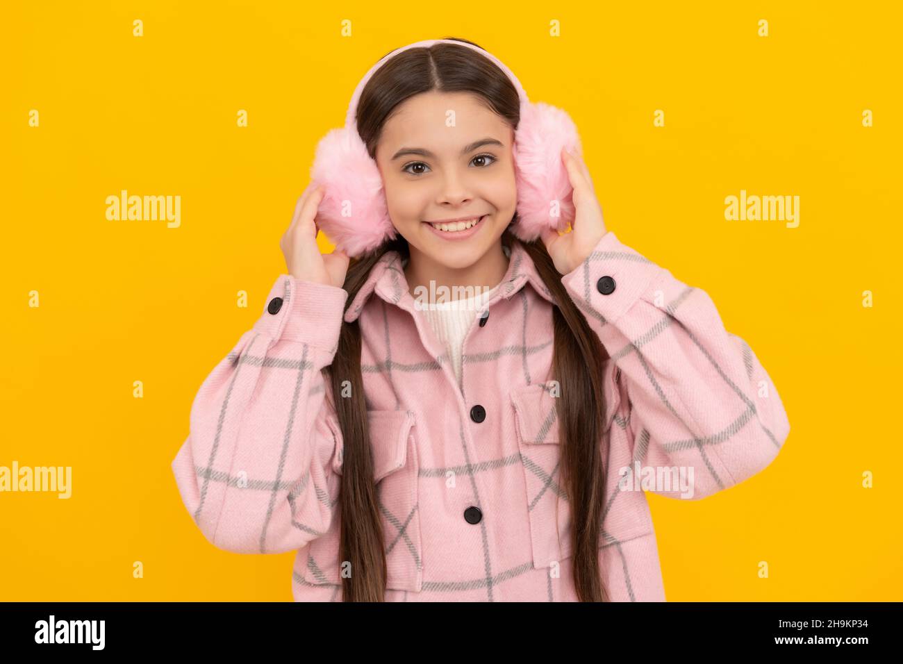Happy Kid Lächeln in warmen Winterkleidung und Fell Ohrwärmer gelben Hintergrund, Ohrenschützer Stockfoto