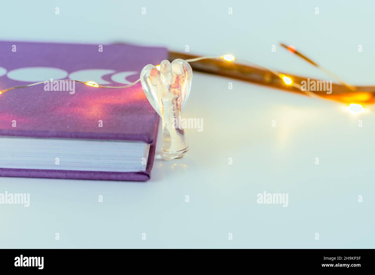 Nahaufnahme von Engelskristall aus klarem Quarz in der Nähe eines Mondjournals mit Weihnachtslichtern und Weihrauch auf dem Hintergrund. Konzept: Spirituelle Selbstversorger-Praktiken Stockfoto