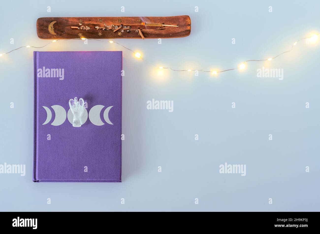 Flaches Mondtagebuch mit Engel-Quarzkristall und brennendem Weihrauch auf weißem Hintergrund mit Kopierraum und Weihnachtslichtern Stockfoto