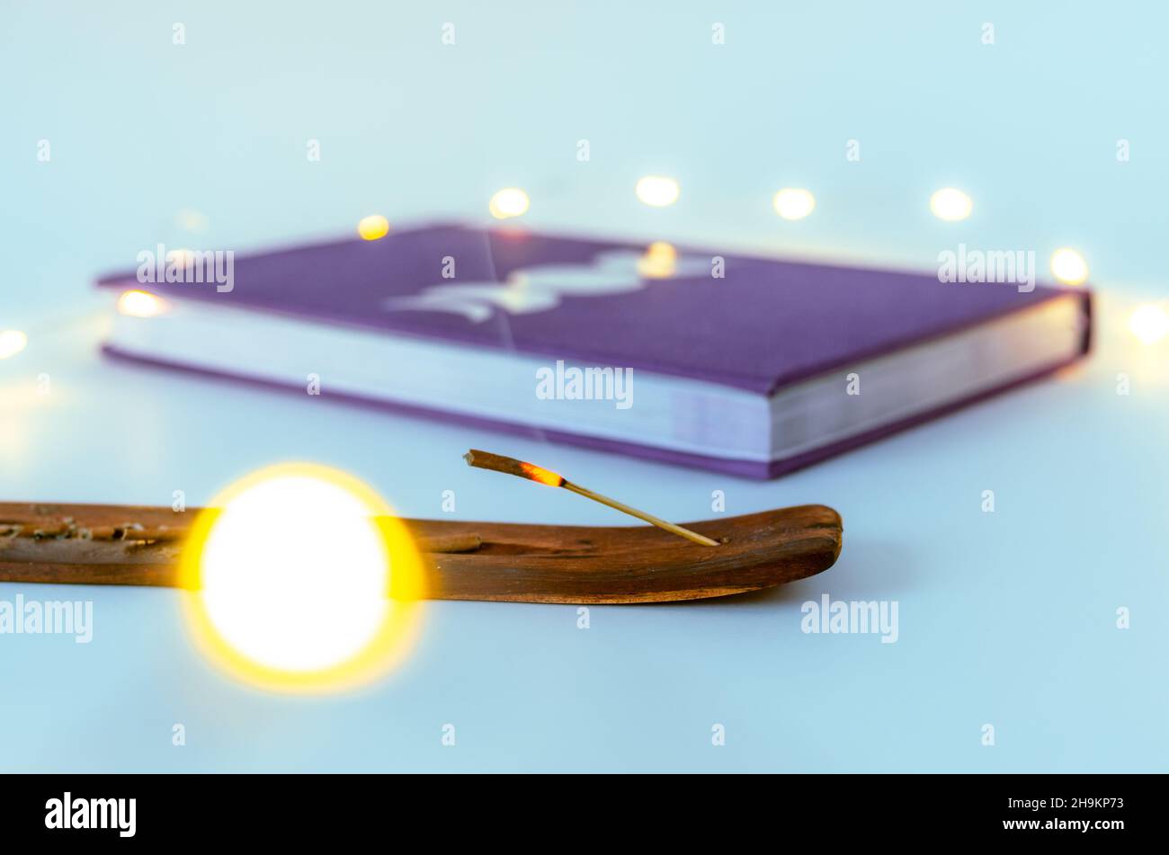 Nahaufnahme des Räucherstäbchenbrennens mit einem Mondjournal mit Weihnachtslichtern im Hintergrund. Konzept: Spirituelle Selbstversorger-Praktiken Stockfoto