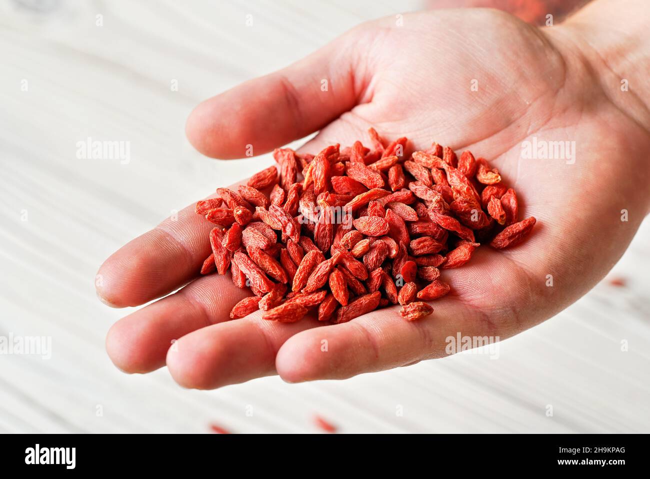Junger Mann mit getrockneten Goji-Beeren über dem Schreibtisch mit weißen Brettern, Details aus der Nähe Stockfoto