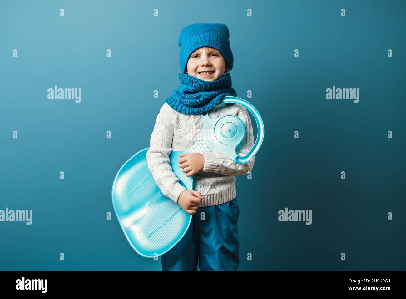 Kleiner Junge mit slad in den Händen. Wintersport- und Freizeitkonzept, Studioaufnahme auf hellblauem Hintergrund. Stockfoto