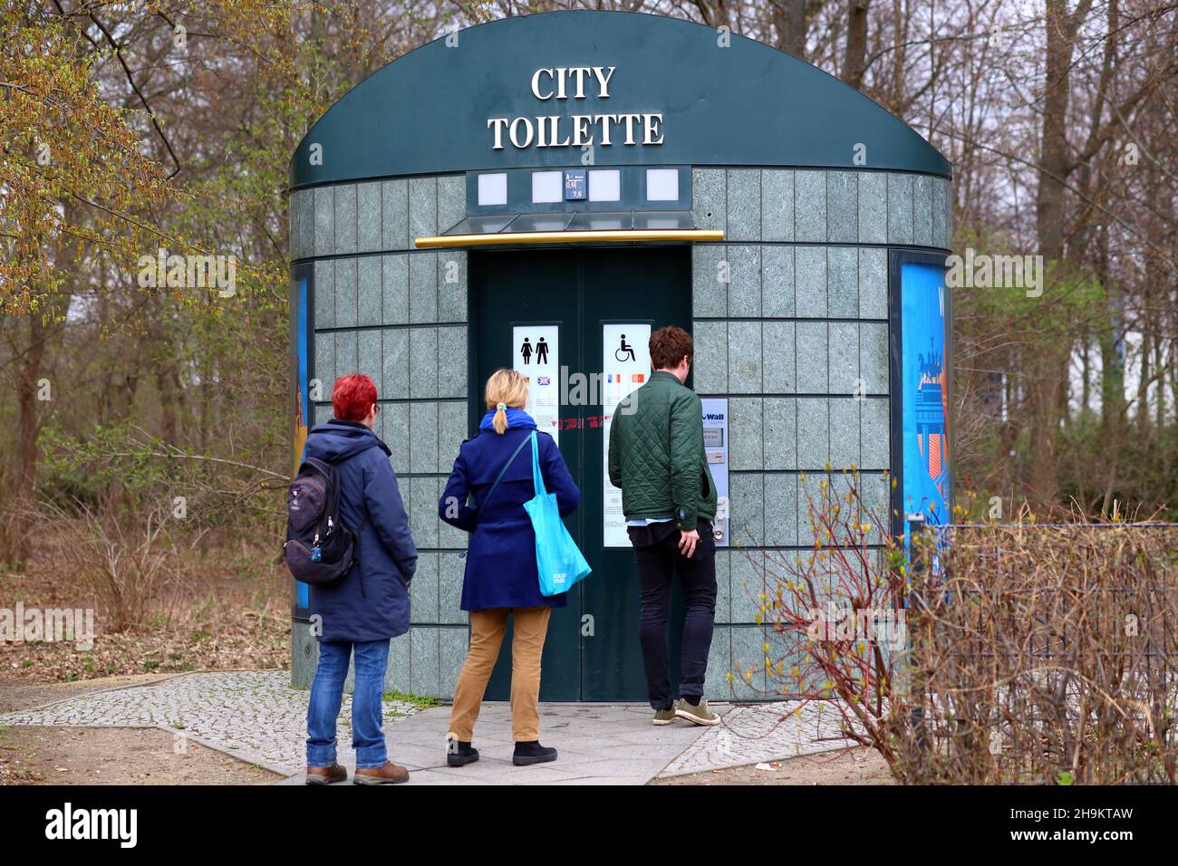 Leute schwirren an einer automatischen Selbstreinigungs-„City Toilette“ in Berlin. Die öffentlichen Toiletten sind kostenpflichtige Toiletten, für die eine Gebühr erhoben wird. Stockfoto