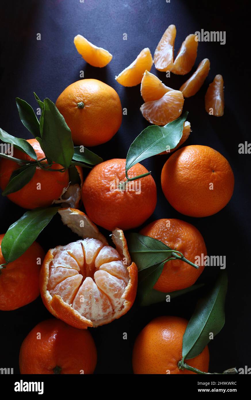 Frische Mandarinen mit grünem Blatt isoliert auf dunklem Hintergrund. Direkt darüber. Stockfoto